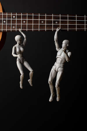 People hang on a ukulele string. The woman and the man hold tight to the string. On a dark background. Music in our hearts.の写真素材