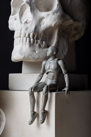 A man sits near a plaster skull on a white cube and looks into the distance. Composition in the dark key.の写真素材