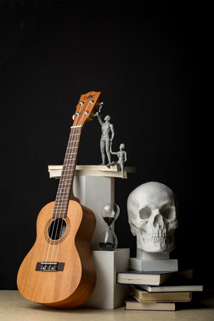 A man, holding a woman's hand, reaches for the ukulele neck. A woman sits on books with her leg dangling down. Nearby are an hourglass and a plaster skull on a stack of books. Vertical composition in a dark key.の写真素材