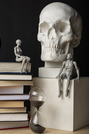A man sits on a plaster cube near the skull. A woman sits on a stack of books near the clock. The couple exchanged glances. Composition in the dark key.の写真素材