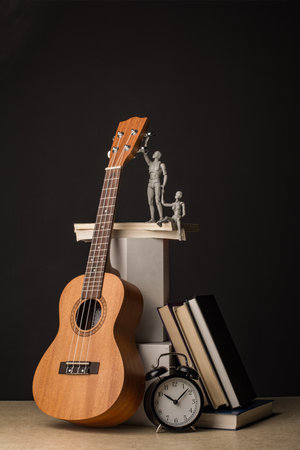 A man, holding a woman's hand, reaches for the ukulele neck. Nearby are stacks of books and clocks. Vertical composition in a dark key.の写真素材