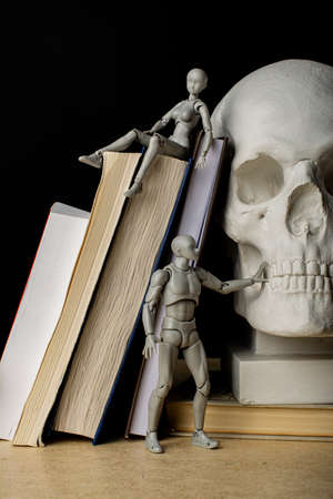 A woman lies on a pile of books, a man stands next to him touching a plaster skull. Composition in the dark key.の写真素材