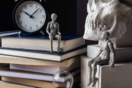 A man sits on a plaster cube near the skull. A woman sits on a stack of books near the clock. The couple exchanged glances. Composition in the dark key.の写真素材