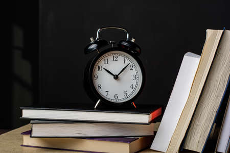 Clock next to a stack of books. time to read. Composition in the dark key.の写真素材