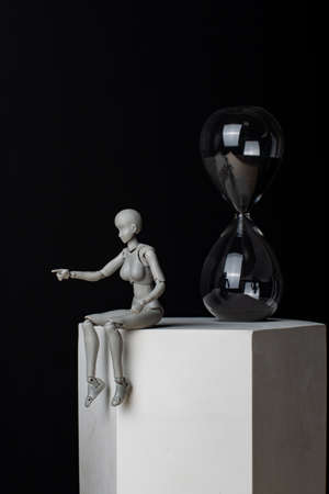 A woman sitting on a plaster prism indicates the direction. The hourglass is behind. Composition in the dark key.の写真素材