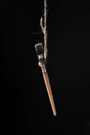 Paintbrush hanging on a rope on a black backgroundの写真素材
