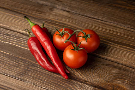 Ripe tomatoes and chili peppers lie on an oak table.の写真素材