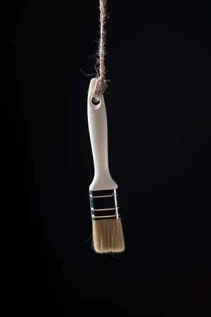 Paintbrush hanging on a rope on a black backgroundの写真素材