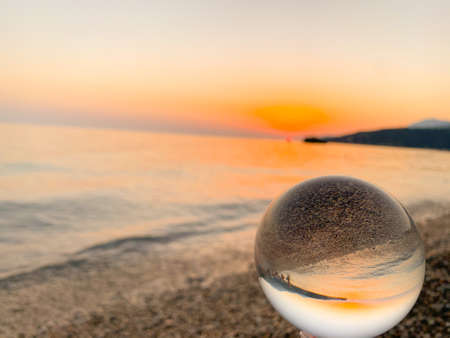 Beautiful sunset view through lens of crystal ball on water horizonの写真素材