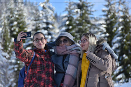 Three young female friends enjoying taking selfies outdoors in winter park.のeditorial素材