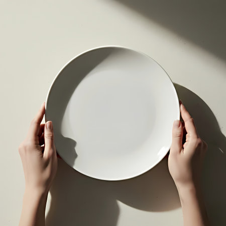 Empty plate in female hands on a light background. Top view.の素材