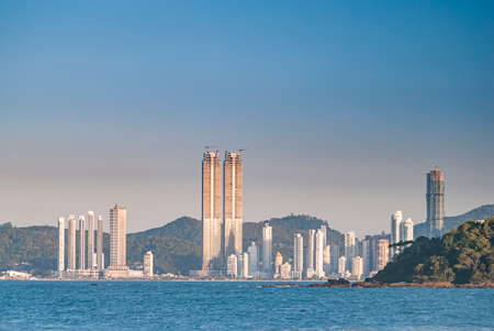 Buildings of the city of BalneÃ¡rio CamboriÃº in front of the sea, with sea and island in the foreground and hill with Atlantic Forest in the background.の写真素材