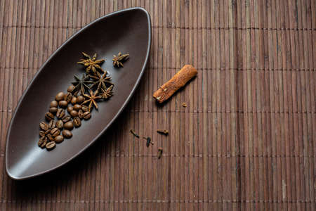 Brown canoe-shaped dish on bamboo mat with coffee beans, star anise, cloves and cinnamon.の写真素材