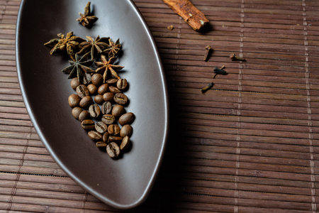 Brown canoe-shaped dish on bamboo mat with coffee beans, star anise, cloves and cinnamon.の写真素材