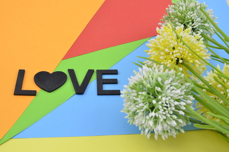 romantic look with black word love and symbol made fromm wood.three artificial circle yellow, green and white flower on colourfull backgroundの写真素材
