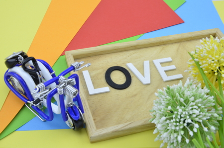 white word and black O on colourfull background.green, yellow and white artificial flower placed on right.wired handcraft scooter with blue color placed on leftの写真素材
