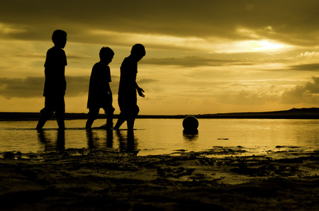 image silhoutte  three boys walking toward the ball on water. sunset sunrise and reflection on waterの写真素材
