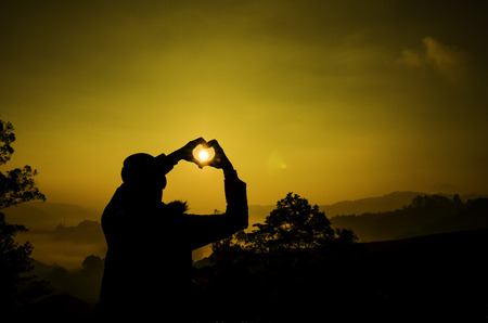 silhouette image a man create love symbol with hand and sunlight during sunset sunriseの写真素材