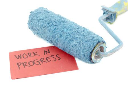 cropped image roller paint brush in blue color. word work in progress printed on red paper isolated white backgroundの写真素材