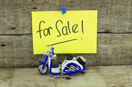 vantage look handwriting with blur word "for sale" on yellow sticky paper. old wood plank with textures background and handcrafted blue wired scooter in the middleの写真素材