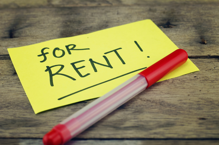 hand writing sign, "for rent" written on yellow sticky paper. dark wooden background with texture. red pen on bottom rightの写真素材