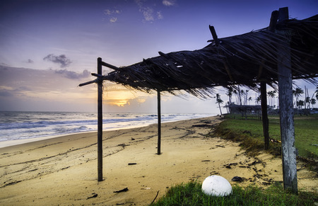 traditional fisherman hut made from coconut leaves near the shore. sand and dramatic cloud during sunriseの写真素材