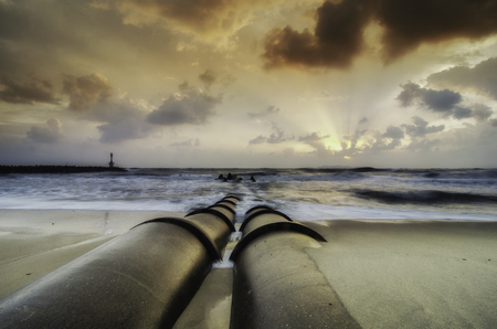 the beauty sunrise at the coastline. concrete drainage pipe at the beach. dark and dramatic clouds...