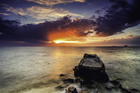 beautiful sunset at the coastline with concrete structure on the beach, dramatic clouds and ray of light  at horizon lineの写真素材