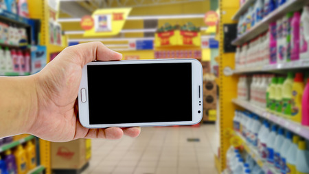image concept, cropped hand holding smartphone over blurred hypermarket backgroundの写真素材