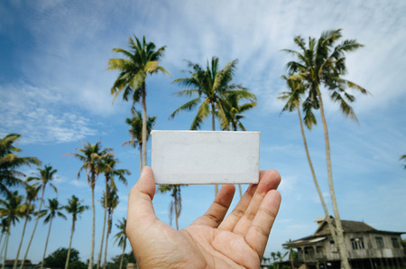 conceptual image, cropped hand holding white frame canvas over blurred village background. color toning effect appliedの写真素材