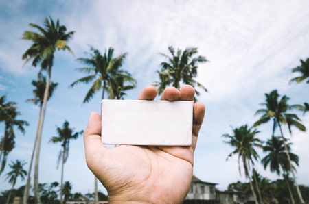 conceptual image, cropped hand holding white frame canvas over blurred village background. color tone appliedの写真素材