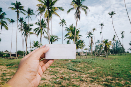 conceptual image, cropped hand holding white frame canvas over blurred village background. color tone appliedの写真素材