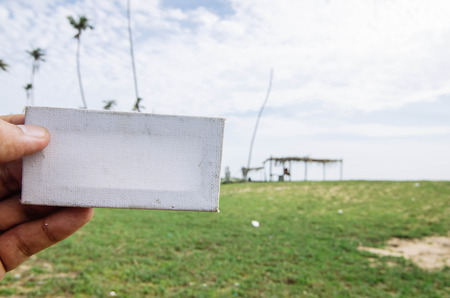 conceptual image, cropped hand holding white frame canvas over blurred village background. color...