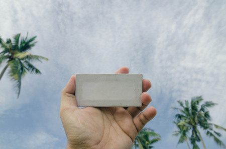 conceptual image, cropped hand holding white frame canvas over blurred village background. color...