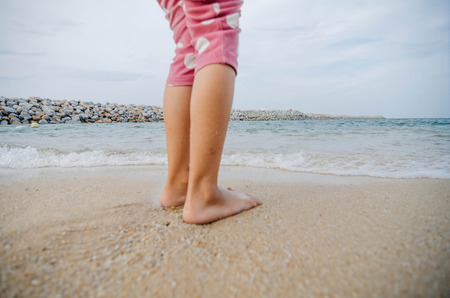 cropped kid leg on the seashore over soft wave and water break. back focused imageの写真素材