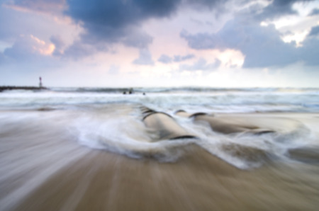blurred image of stunning sunrise scenery at the beach.soft waves hitting concrete drainage pipe.の写真素材