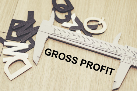 Business motivation and finance concept, vernier calliper with word GROSS PROFIT over wooden floor and alphabetical word made from wood backgroundの写真素材