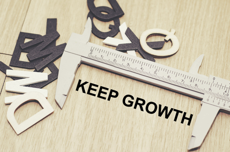 Business motivation and finance concept, vernier caliper with word KEEP GROWTH over wooden floor and alphabetical word made from wood backgroundの写真素材