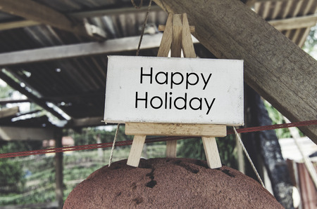 concept image, word HAPPY HOLIDAY on cropped red buoy over blurred background. wooden hut with faded color tone effectの写真素材