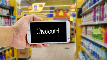 image concept, cropped hand holding smartphone with word DISCOUNT over blurred hypermarket backgroundの写真素材