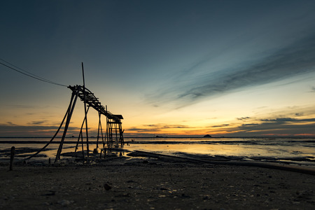 Golden Hour moment,beautiful tropical sunset background, wooden water pump tower on the muddy beach. cloudy and yellow sky.surface level shot.low tide sea viewの写真素材
