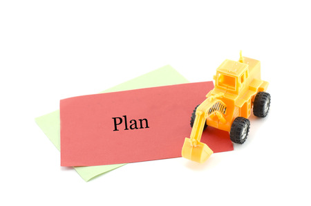 image concept yellow toy bulldozer on red paper with word PLAN. isolated white background