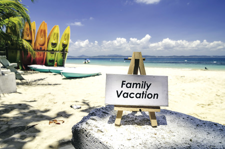 white canvas frame and wooden easel with word FAMILY VACATION. Tropical beach  at sunny day ,white sand,colorful kayaks and clear blue water background.の写真素材