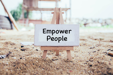 conceptual image with word EMPOWER PEOPLE on white canvas and wooden easel over blurred background. sandy foreground at sunny dayの写真素材
