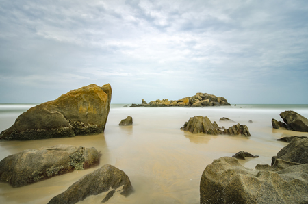 Stunning sea view of tropical beach. Wet Rock and crystal clear sea water with cloudy sky background.blurred and soft focus image due to long exposure shotの写真素材
