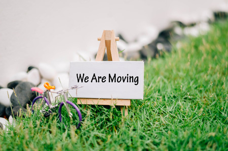 conceptual image with word "we are moving" over blurred image and retro look ,handcrafted bicycle made from colorfull wired. white canvas frame on wooden easel and green grassの写真素材
