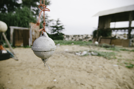 selective focus grey color buoy tied with red rope, hanging under wooden cottage over blurred sandy beach backgroundの写真素材