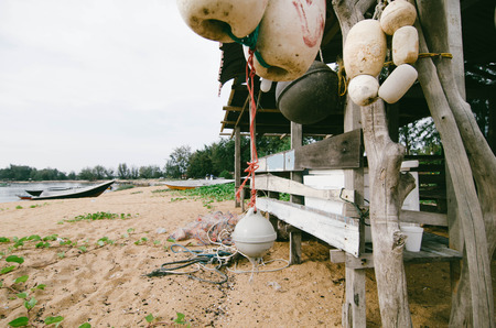 seashore scenery at Terengganu, Malaysia. Dirty white fish net buoy hanging under wooden cottage on the sandy beach.fisherman boat anchored during low tide waterの写真素材