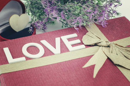 word LOVE made from wood on red gift box with ribbon made from recycle paper.artificial flower and ring case.retro color tone effectの写真素材