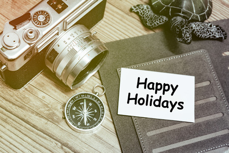 Business travel concept image, word Happy Holiday on name card, personal planner book, vintage camera,compas and wooden floor backgroundの写真素材